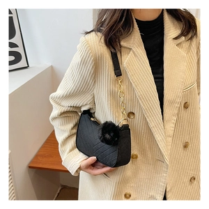 Détail du sac sous le bras en feutre noir matelassé avec chaîne dorée et pompon en fourrure