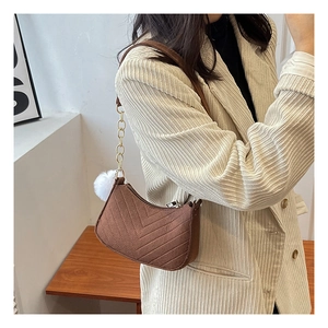 Détail du sac bandoulière en daim marron avec matelassage en V et pompon en fourrure blanche