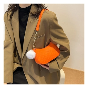 Détail du sac demi-lune orange avec chaîne dorée et pendentif pompon blanc soyeux