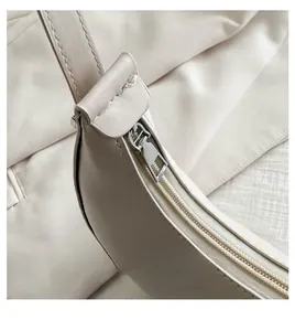 Detailed macro view of the smooth silver metal zipper and neat stitching on a cream underarm bag