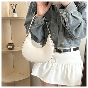 Close-up of a white crescent underarm bag with smooth leather finish on a wooden shelf