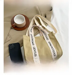 Dettaglio della borsa tote in tela con tracolla a contrasto logata su un blazer beige