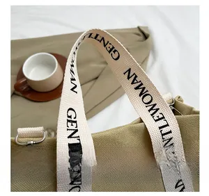 Dettaglio della tracolla in tessuto bianco con scritte nere su una borsa tote in tela khaki