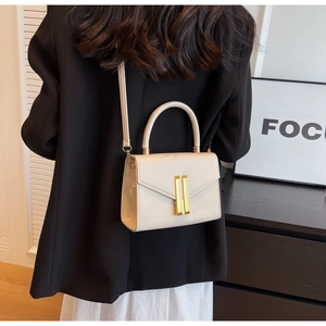 Detail view of cream crossbody bag with gold lock hardware on a model's shoulder
