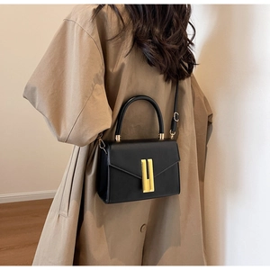 Close-up of a black leather crossbody bag worn by a model in a trench coat