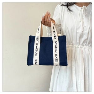 Dettaglio borsa tote in tela blu navy con manici crema e scritta Gentle Woman