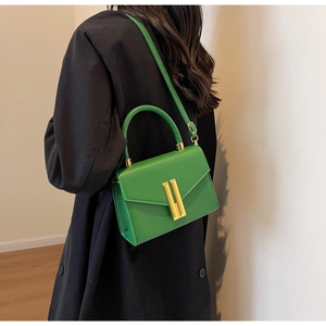 Chic green leather crossbody bag with gold buckle styled on a black coat outfit