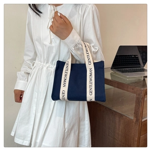 Piccola borsa tote in tela blu scuro con manici logo tenuta da una modella