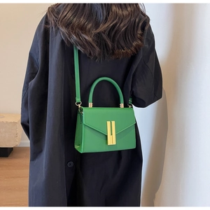 Close-up of vibrant green handbag with gold bar lock and leather texture on black coat
