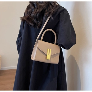 Chic beige crossbody handbag with golden buckle and top handle worn by a model