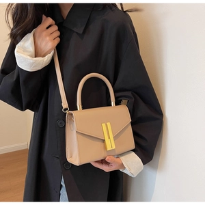 Detail shot of beige flap handbag with gold metal lock bars and leather shoulder strap
