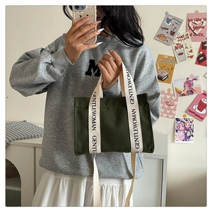 Dettaglio borsa in tela verde scuro con scritte GENTLEWOMAN sui manici e tracolla inclusa