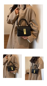 Detail view of black leather handbag featuring a golden H-shaped metal buckle and strap