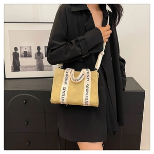 Dettaglio della borsa tote in tela verde chiaro con testo GENTLEWOMAN sulle maniglie