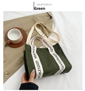 Dettaglio della borsa tote in tela verde con tracolle a contrasto e scritte con logo