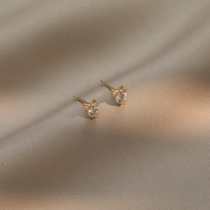 Orecchini a fiocco dorati con zircone a cuore su sfondo di seta champagne