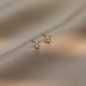 Eleganti orecchini a fiocco dorati con zircone a cuore su sfondo di raso