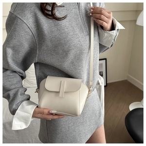 Detailed view of cream white crossbody bag with vertical strap detail on model in home setting