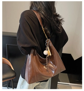 Detail view of large brown leather tote bag with baseball charm and metal chain strap