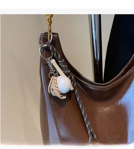 Detail of brown glossy leather tote bag with unique baseball themed pendant and woven strap
