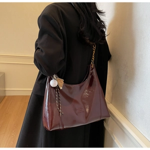 Detail of dark red glossy hobo bag with metal chain strap and creative baseball charms