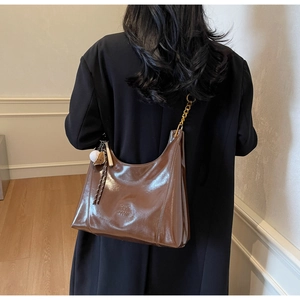 Close-up of brown glossy leather hobo bag with gold chain strap and tassel detail