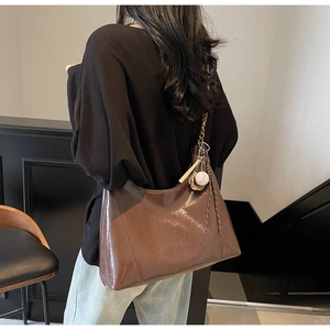 Detail of dark brown tote bag with gold chain and baseball charm on a model