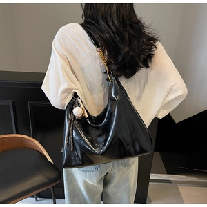 Detail of black patent leather tote bag with gold chain strap and baseball pendant