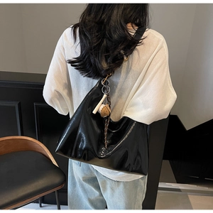Detail of glossy black leather tote bag with unique charms on model back view