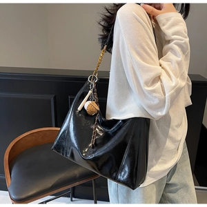 Detail of glossy black hobo bag with gold chain and baseball themed pendants on a model