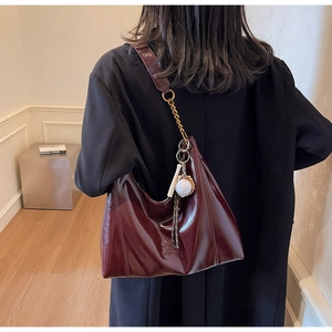 Detail of burgundy glossy tote bag with stylish baseball charm and chain shoulder strap