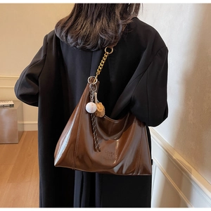Detail view of large brown hobo bag featuring a gold chain and a baseball glove charm