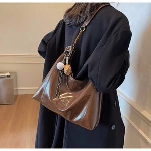 Detail of dark brown glossy leather hobo bag with gold chain strap and baseball charms