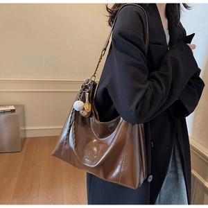 Detail of a brown leather tote bag featuring a baseball charm and metal chain strap