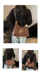 Close-up of dark brown glossy underarm bag with gold chain and plush ball pendant charm