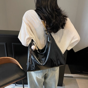 Large black glossy hobo bag with gold chain strap shown on model for daily commuting