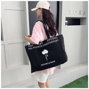 Close-up of black canvas tote bag featuring minimalist white flower print and logo text