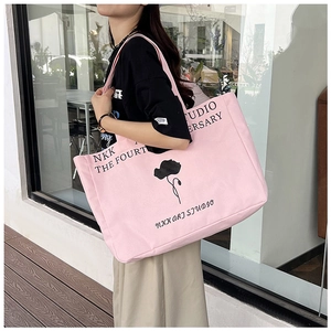 Detailed street style shot of a pink canvas tote bag with black floral art and text