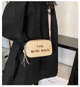 Detail of beige mini crossbody bag with wide strap and tassel worn with black coat