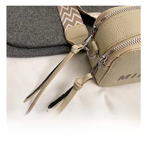 Detail of silver metal hook and woven strap on beige pebbled leather camera bag