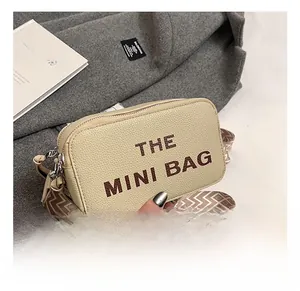 Detail of beige litchi grain mini bag with bold brown lettering and patterned strap