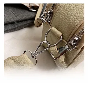 Detail of silver metal hook and textured lychee leather on a beige shoulder bag