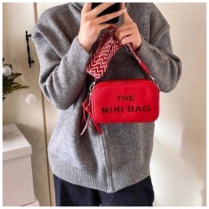 Model wearing a red leather camera bag with a geometric wide strap and tassel detail