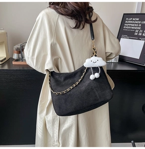 Détail d'un sac cabas en daim noir avec chaîne dorée et pendentif en peluche blanche