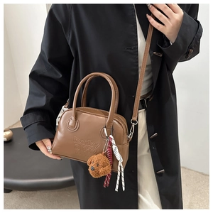 Close-up of brown leather handbag featuring embossed lettering and a cute teddy charm