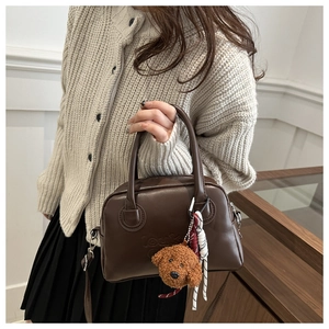 Detail of vintage brown leather Boston bag with plush dog charm and braided cord accessory