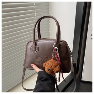 Detail of dark coffee Boston bag with embossed logo and plush puppy charm