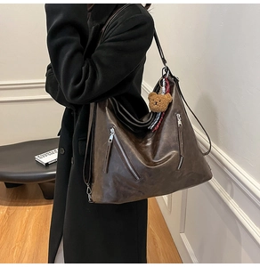 Detail of dark brown leather tote bag with side zippers and a cute teddy bear charm