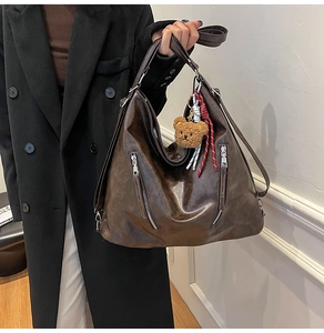 Detail of vintage brown leather tote bag with metallic zippers and bear pendant charm