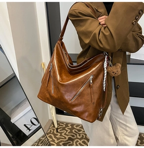 Detail of a large brown leather tote bag with glossy finish and plush bear charm decoration